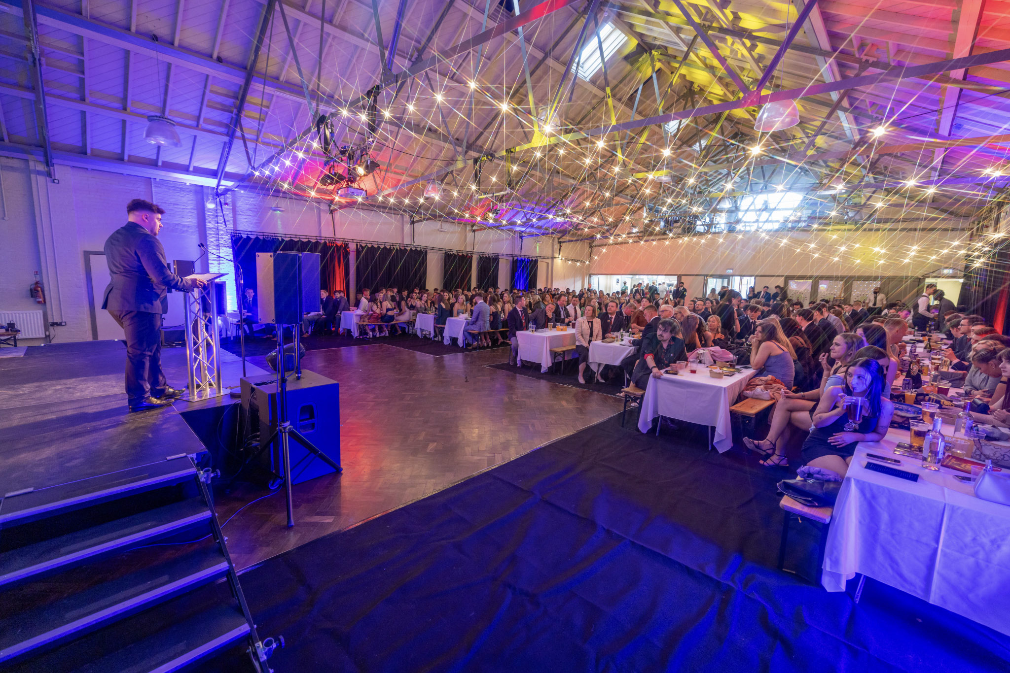 A party event at Westgate Hall showing a stage, colourful lighting and people eating.